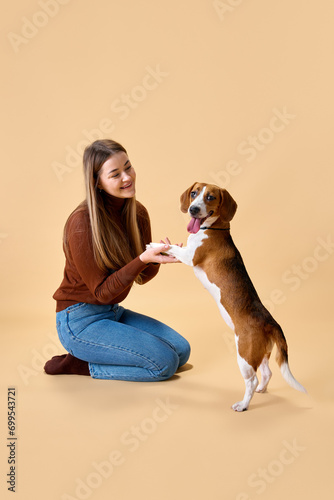 Wallpaper Mural Happy time with pet. Female model having fun with her lovely pet, purebred Beegle against beige background. Concept of animal, pet lover, friendship, domestic life, companionship. Torontodigital.ca