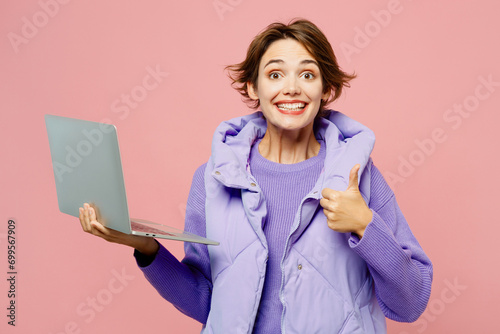 Young amazed happy IT woman wearing purple vest sweatshirt casual clothes hold use working on laptop pc computer show thumb up isolated on plain pastel light pink background studio. Lifestyle concept. photo