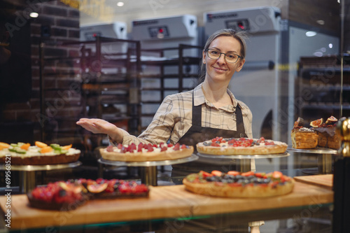 Young happy seller consultant woman wear uniform working at supermaket store grocery shop stand near sweet pastry show bakery products selling inside hypermarket. Purchasing food gastronomy concept © ViDi Studio