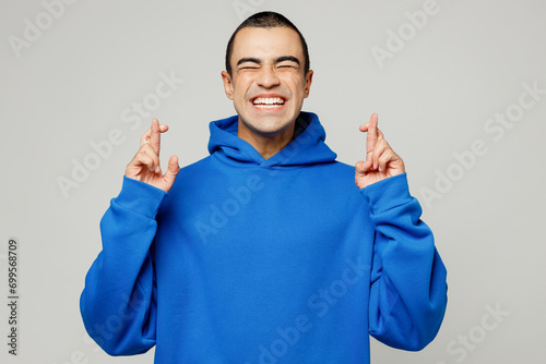 Young worried middle eastern man wear blue hoody casual clothes waiting for special moment, keeping fingers crossed, making wish closed eyes isolated on plain solid white background studio portrait photo