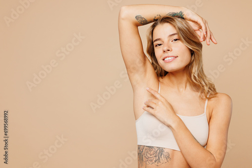 Close up young nice lady woman with slim body perfect skin wearing nude top bra lingerie stand raise up hand touch armpit isolated on plain pastel light beige background. Lifestyle diet fit concept. photo