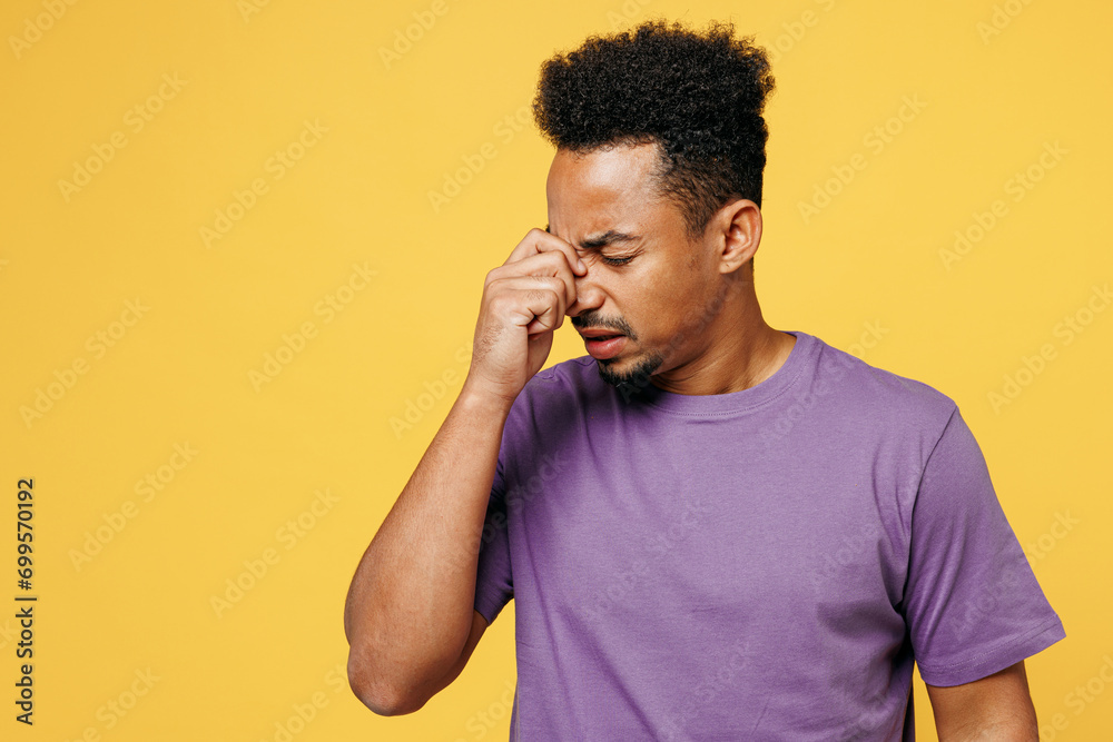 Young sad sick ill tired man of African American ethnicity he wears purple t-shirt casual clothes keep eyes closed rub put hand on nose isolated on plain yellow background studio. Lifestyle concept. Young sad sick ill tired man of African American ethnicity he wears purple t-shirt casual clothes keep eyes closed rub put hand on nose isolated on plain yellow background studio. Lifestyle concept.
