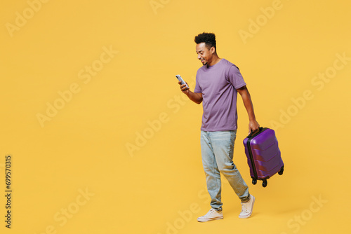 Traveler man wears casual clothes hold bag suitcase use mobile cell phone isolated on plain yellow background. Tourist travel abroad in free spare time rest getaway. Air flight trip journey concept. #699570315