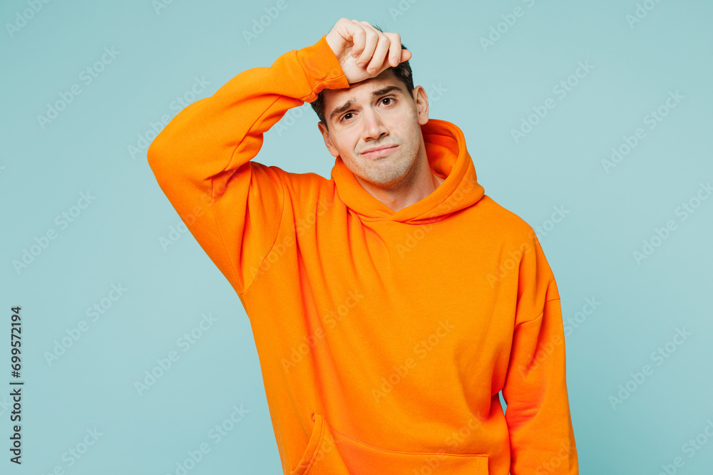 Young sad sick exhausted upset man he wears orange hoody casual clothes put hand on forehead look camera isolated on plain pastel light blue cyan color background studio portrait. Lifestyle concept. Young sad sick exhausted upset man he wears orange hoody casual clothes put hand on forehead look camera isolated on plain pastel light blue cyan color background studio portrait. Lifestyle concept.