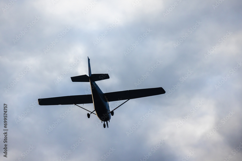 Light aircraft silhouette is in cloudy sky on a daytime, rear view Light aircraft silhouette is in cloudy sky on a daytime, rear view