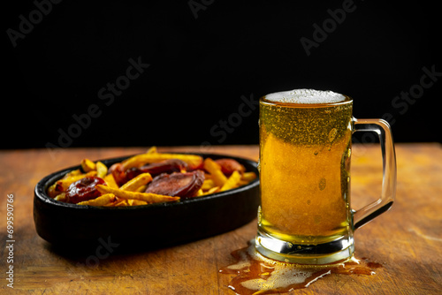 foam in a glass with beer and fried sausages with potatoes on a wooden background.Oktoberfest.