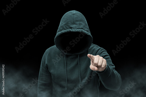 Mysterious faceless hooded anonymous criminal, silhouette of computer hacker, cyber terrorist or gangster on black background with smoke