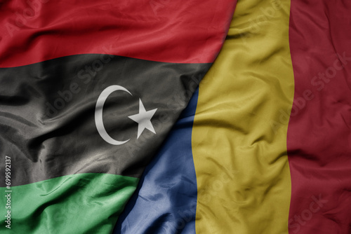 big waving national colorful flag of romania and national flag of libya .