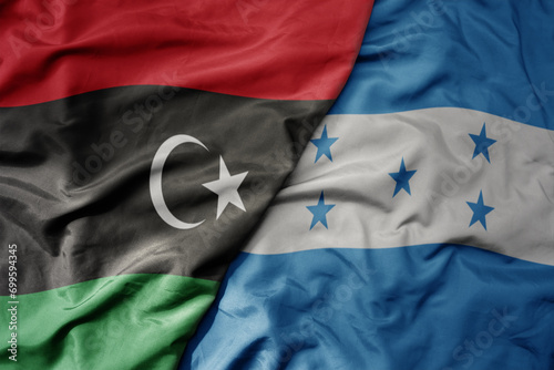 big waving national colorful flag of honduras and national flag of libya .