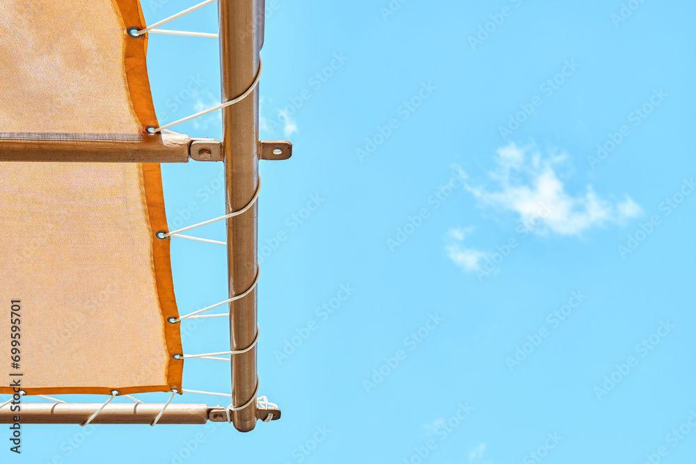 Orange canopy over sun loungers against clear blue sky. Edge of sun-protection cover in recreational area of water park in summer closeup