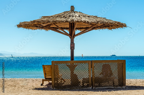 wooden loungers under a bamboo beach umbrella on the beach against the sea and blue sky in Egypt Dahab South Sinai