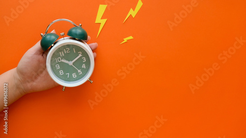 Hand holds ringing classic green alarm clock on orange background with a copy space photo