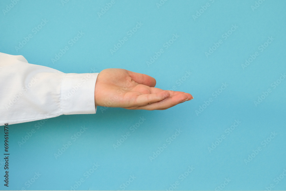 A hand in a white shirt holds something on a blue background