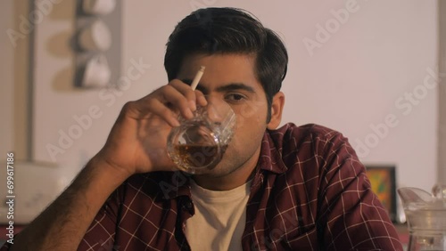 A frustrated Indian youngster drinking and smoking at home - stressed lifestyle  alcohol addict  smoking problem. An unhappy Indian man tired of his life problems - loneliness  addiction and alcoho... photo