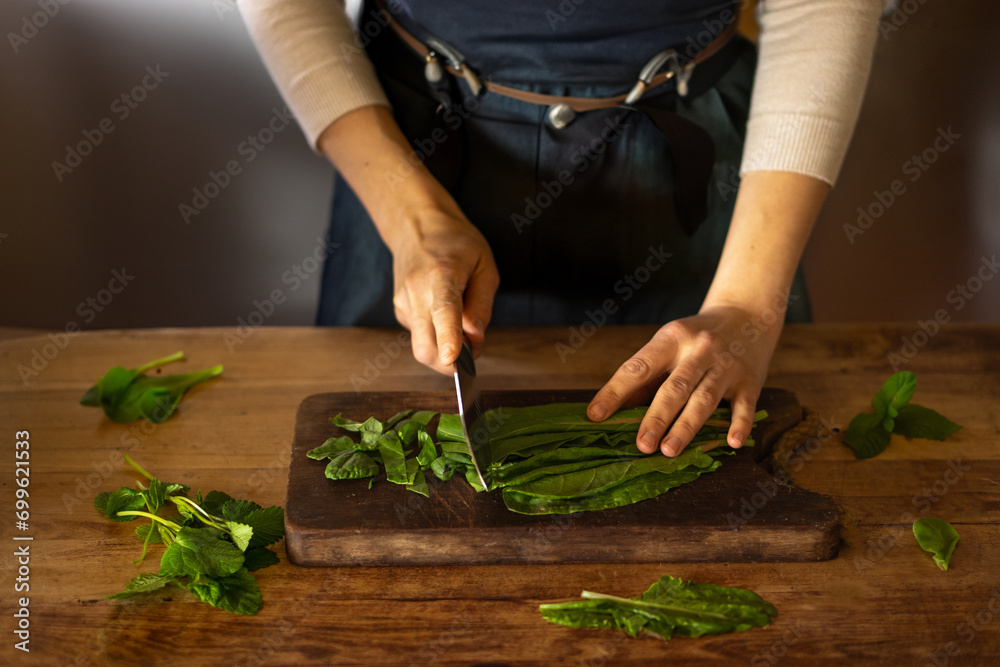 Woman cooking, cutting green salad on wooden table, zoom on hands. High quality photo