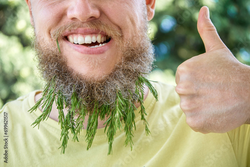 Smiling man beard and fragrant sprig of rosemary. Adult behaving childishly man in sunny meadow with excited expression on face and thumb up closeup photo
