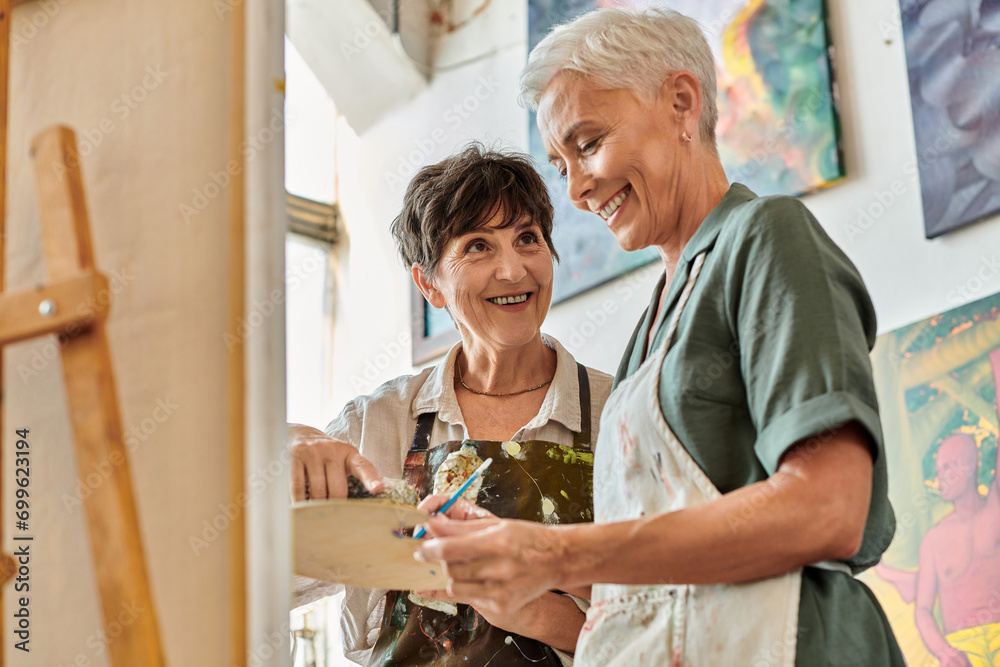 Obraz premium cheerful middle aged female artists mixing paints on palette during master class in art workshop