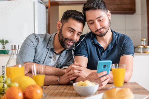 romantic gay couple using mobile phone and watching video together in kitchen table photo