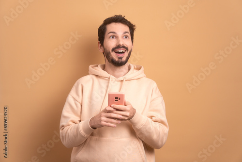 happy bearded man smiling and holding mobile phone in all beige colors. communication, app, connection concept. © Vergani Fotografia