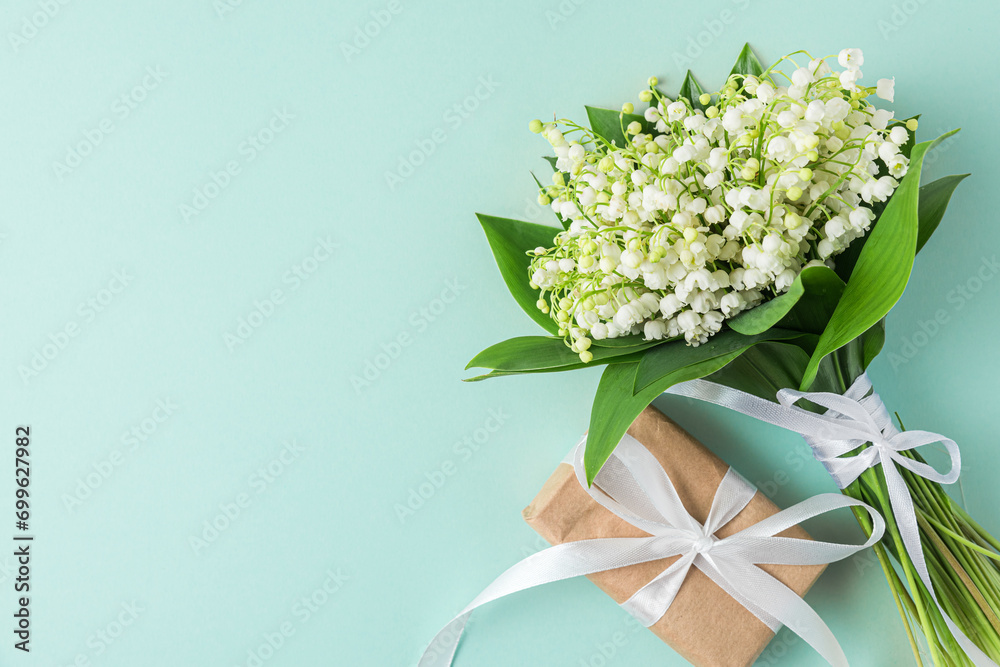 Lily of the valley flowers bouquet with gift box on blue background. Womens day, Valentines day card. Top view with copy space. Flat lay
