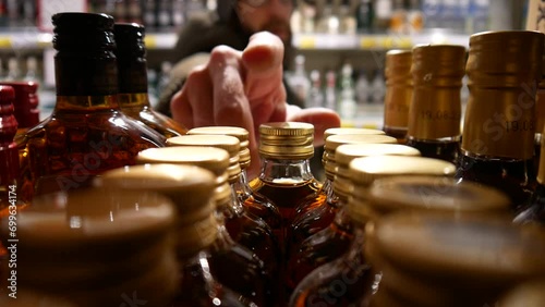 Close-up of many beautiful bottles of whiskey and brandy in alcohol store and a male buyer chooses one. photo