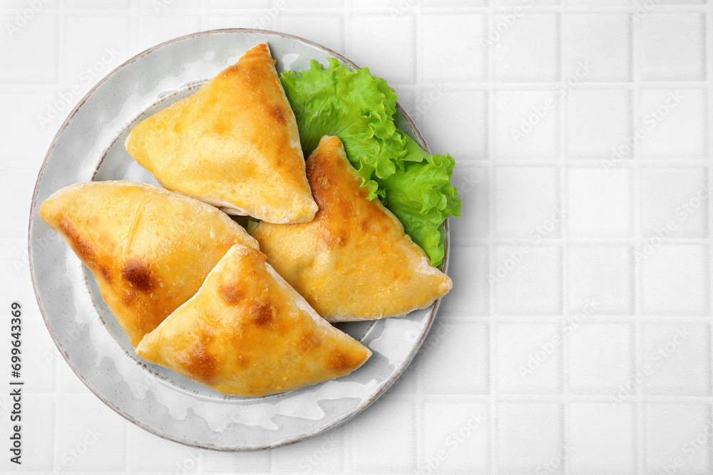 Delicious samosas and lettuce on white tiled table, top view. Space for text