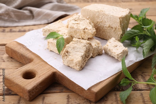 Pieces of tasty halva and mint leaves on wooden table, closeup