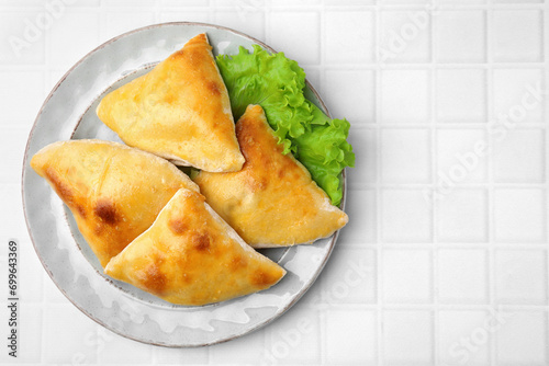 Delicious samosas and lettuce on white tiled table, top view. Space for text