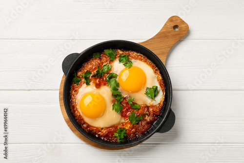 Delicious shakshuka in frying pan on white wooden table, top view photo