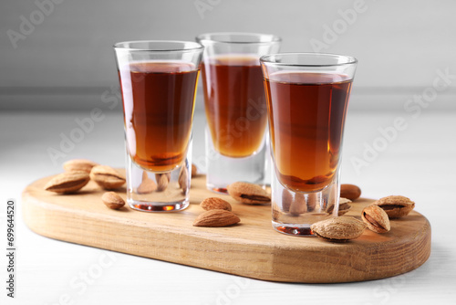 Shot glasses with tasty amaretto liqueur and almonds on white wooden table, closeup