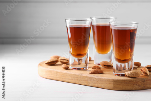 Shot glasses with tasty amaretto liqueur and almonds on white wooden table, closeup. Space for text