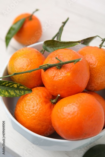 Fresh ripe tangerines and leaves in bowl on white table, closeup