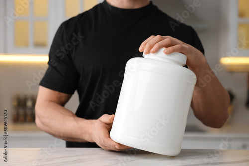 Young man with jar of protein powder at white marble table in kitchen, closeup