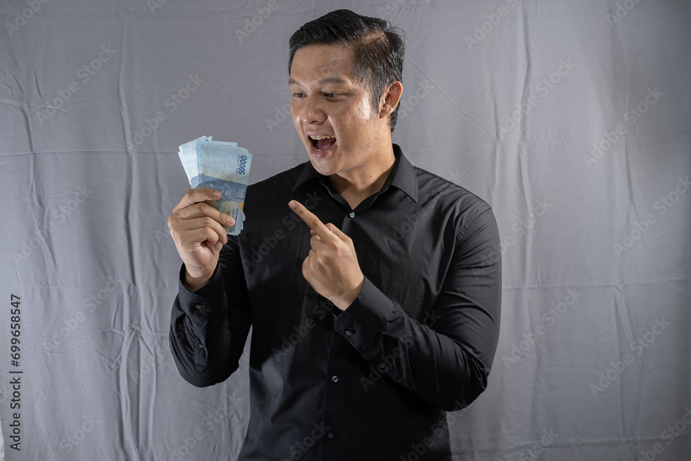 Young Asian businessman holding money with a happy gesture because his business and finances are on the rise Young Asian businessman holding money with a happy gesture because his business and finances are on the rise