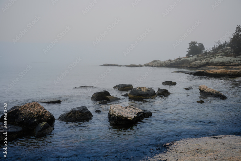 Foggy Seascape with Glacial Stones, misty islands, and hilly cliffs at Rocky Neck Beach State Park of Long Island Sound in Niantic, Connecticut, United States