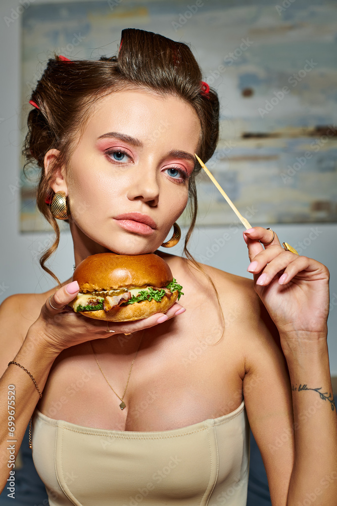 beautiful appealing woman in beige sexy corset holding huge delicious burger and looking at camera beautiful appealing woman in beige sexy corset holding huge delicious burger and looking at camera