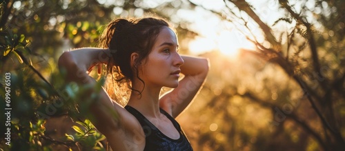 Fit young woman warming up outdoors  stretching arms and glancing away in high key lighting.