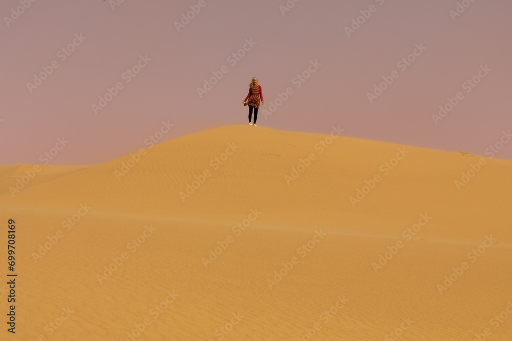 A lone woman in the distance atop a sand dune in the Namib desert in Namibia.