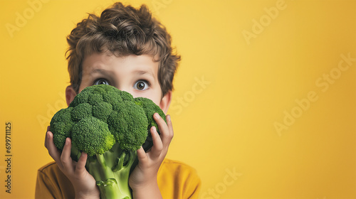 Boy holding a huge broccoli in his hands. Solid yellow background. Copy space. photo