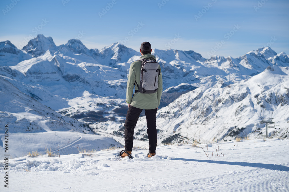 Hombre con ropa de montaña, mochila y raquetas de nieve en lo alto de la montaña mirando la cordillera nevada de la estación de esquí de Candanchú en los Pirineos Aragoneses.