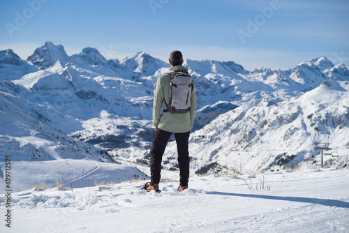 Hombre con ropa de montaña, mochila y raquetas de nieve en lo alto de la montaña mirando la cordillera nevada de la estación de esquí de Candanchú en los Pirineos Aragoneses. © Miguel