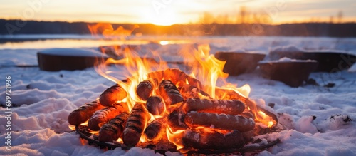 Cooking sausages on a stick over a winter bonfire. Outdoor adventure and seasonal vacation. Vertical. © AkuAku