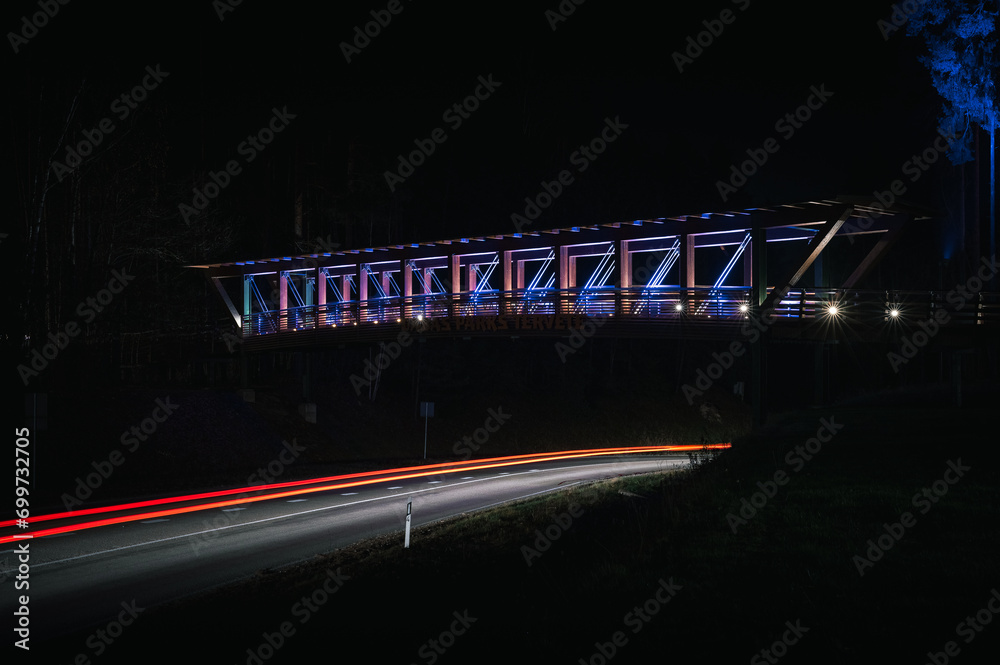 Colorful footbridge leading over a highway at night time. Light trails from car lighting up the road.