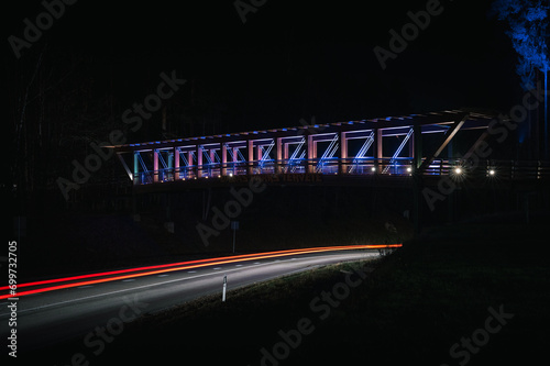 Obraz na płótnie Colorful footbridge leading over a highway at night time. Light trails from car lighting up the road. w salonie