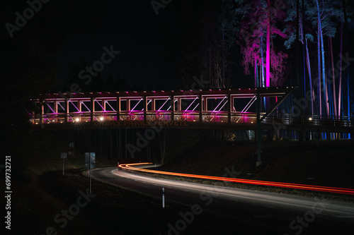 Obraz na płótnie Colorful footbridge leading over a highway at night time. Light trails from car lighting up the road. w salonie