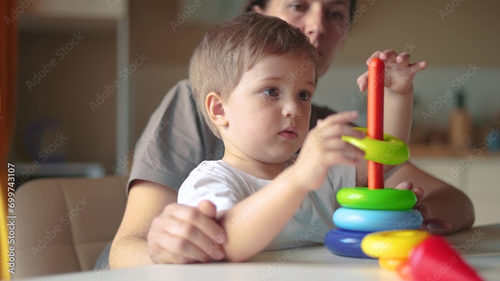 baby baby with mom collects a toy pyramid. happy family kindergarten kid dream concept. mom helps baby son collect a toy pyramid. son learns to lifestyle assemble a toy pyramid in the kindergarten baby baby with mom collects a toy pyramid. happy family kindergarten kid dream concept. mom helps baby son collect a toy pyramid. son learns to lifestyle assemble a toy pyramid in the kindergarten