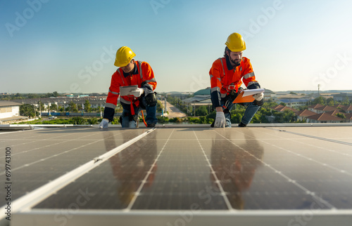 Lower view two Caucasian technician workers hold document pad and tablet check and maintenance the solar panels on rooftop of the building or factory.