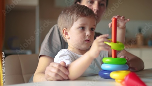 baby baby with mom collects a toy pyramid. happy family kindergarten kid dream concept. mom helps baby son collect a toy pyramid. son learns to lifestyle assemble a toy pyramid in the kindergarten