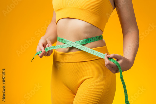 Fitness woman with measure tape isolated on yellow background. Weight loss and healthcare concept