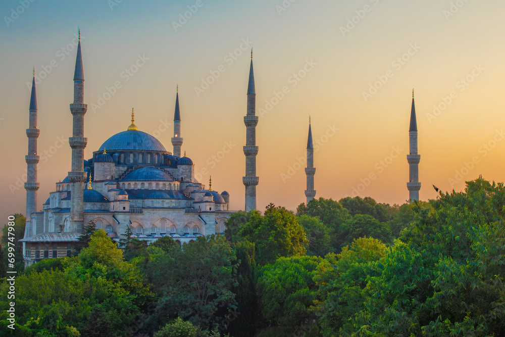 Obraz premium Beautiful view of a the Blue Mosque with towering minarets at sunrise, surrounded by lush greenery. Ideal for themes of culture, history, and spirituality in wall art, home décor, or educational mater